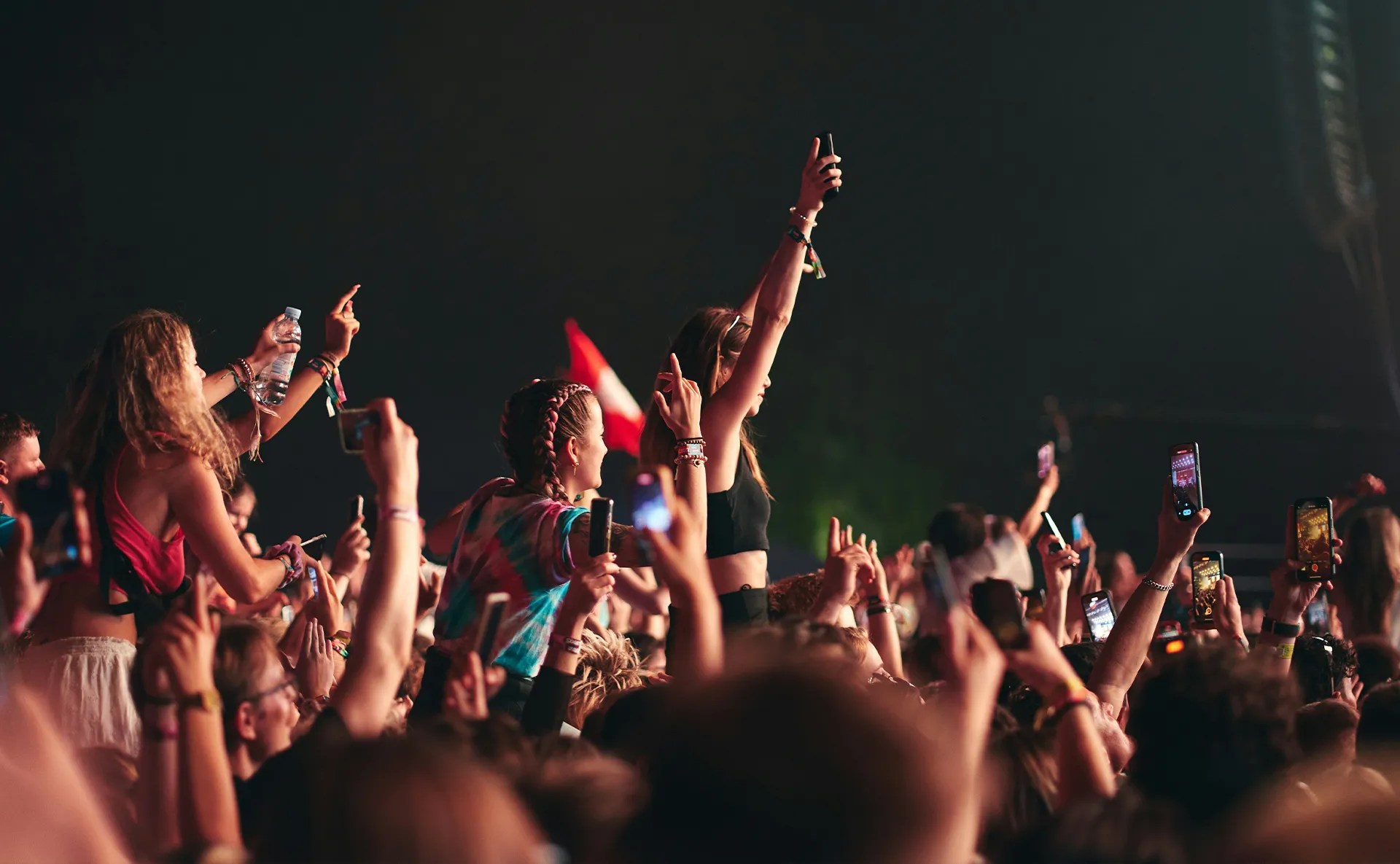 Concertgoers capturing a live performance on their phones at a packed outdoor music festival.