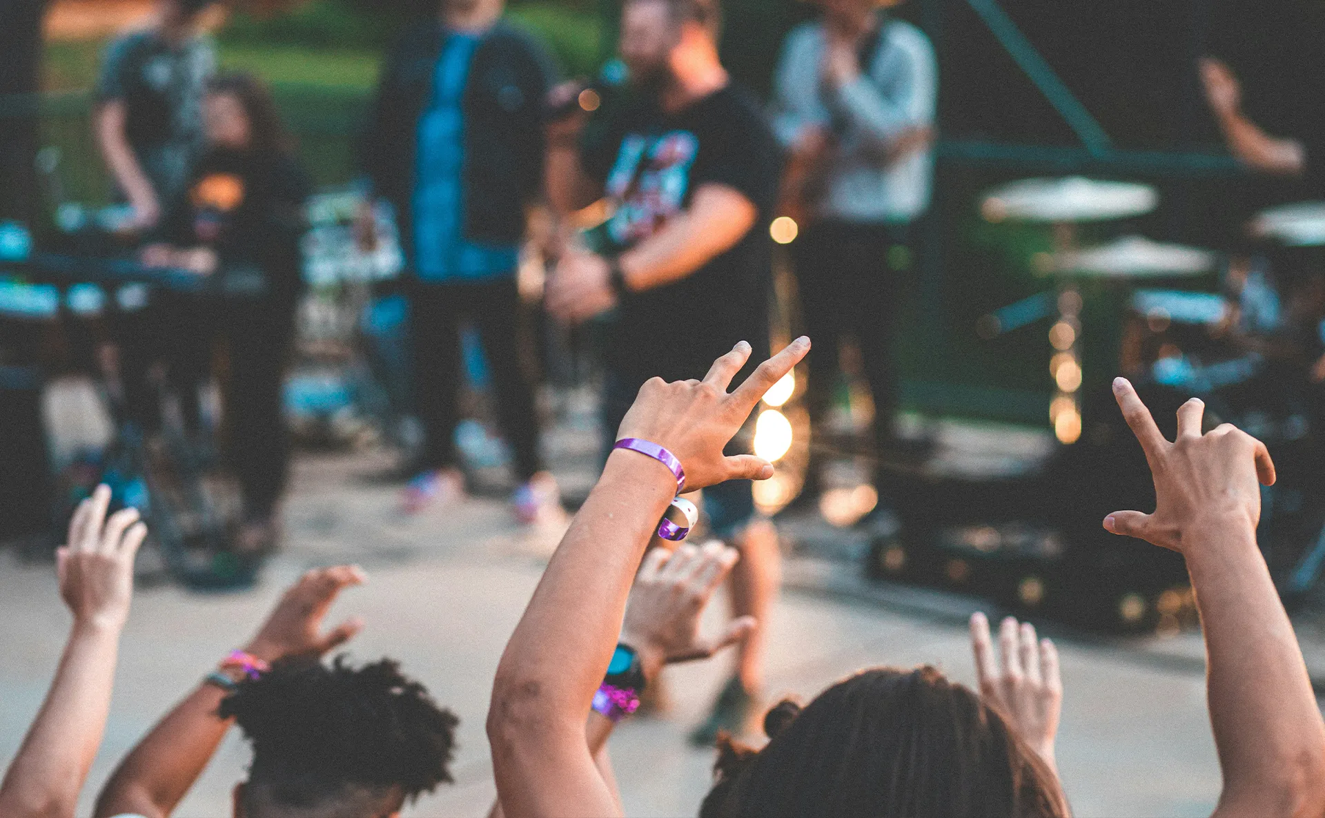 Festival attendees cheering during a live music performance with wristbands and stage lighting in the background.